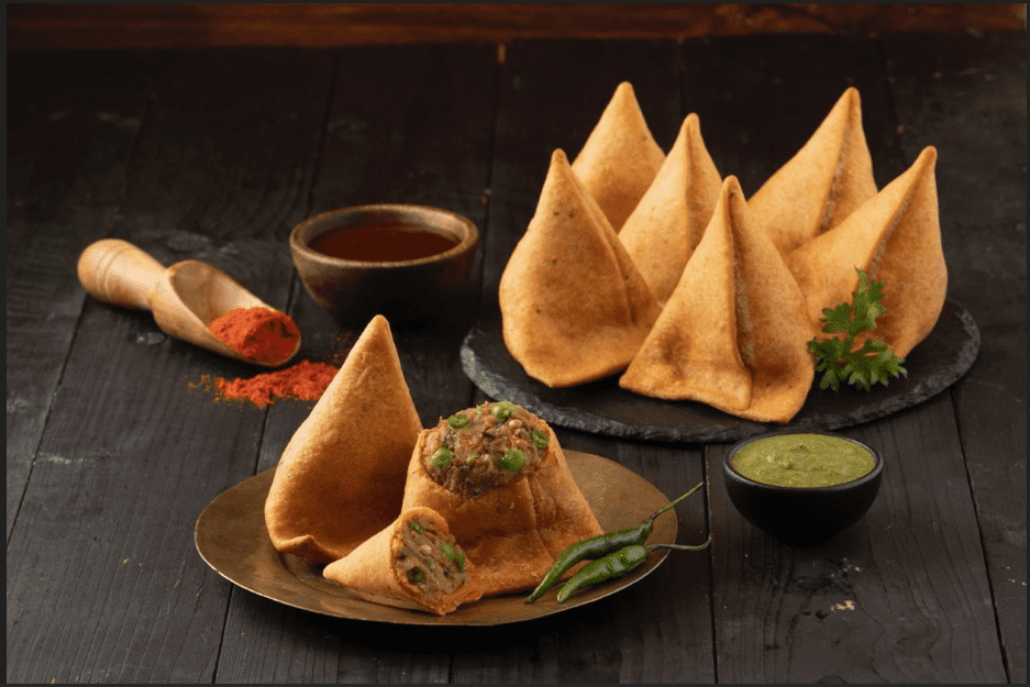 Golden-brown vegetable samosas served with mint and tamarind chutney on a wooden platter.